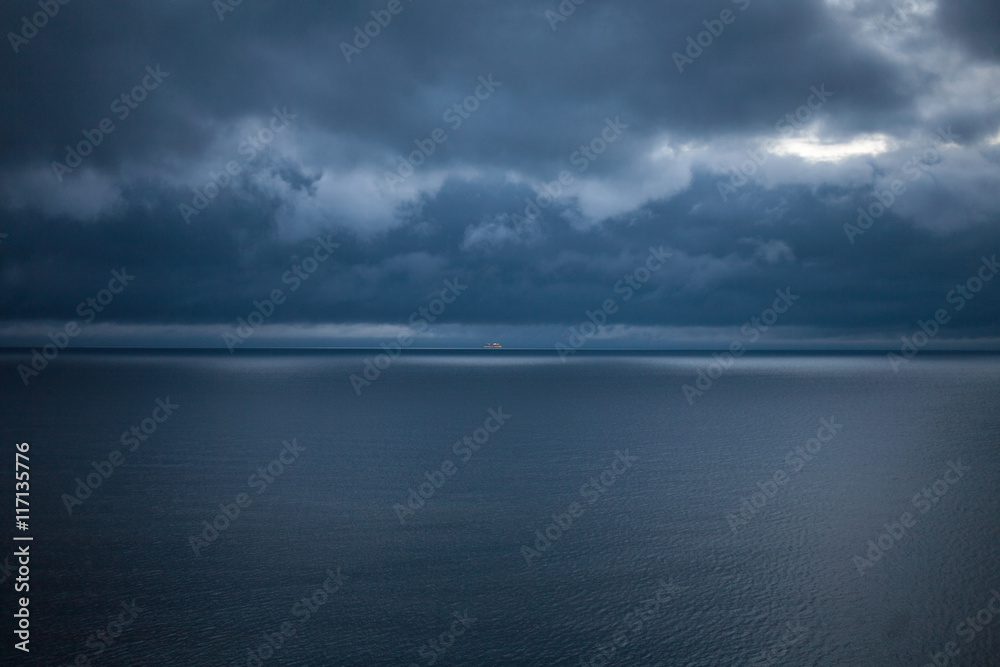 Cruise ship on a dark blue sea under a stormy, cloudy sky