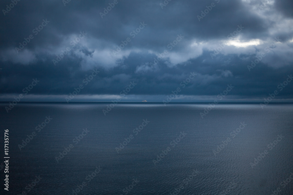 Obraz premium Cruise ship on a dark blue sea under a stormy, cloudy sky