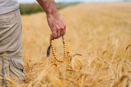 background with hand in wheat field nature outdoors, closeup. Rosary in hand
