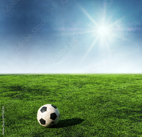 Soccer ball on green grass at soccer field with sunshine on blue sky