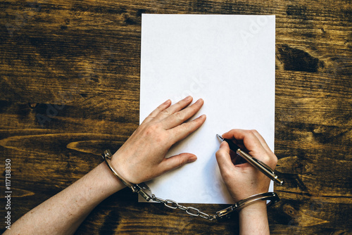 Slika na platnu Female hands cuffed signing confession, top view