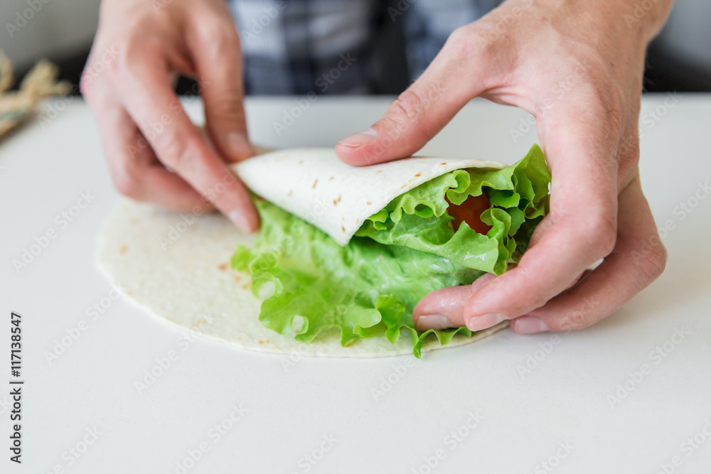 man prepares to roll fast food.
chicken nuggets, lettuce, tomato, cheese, Mexican tortillas