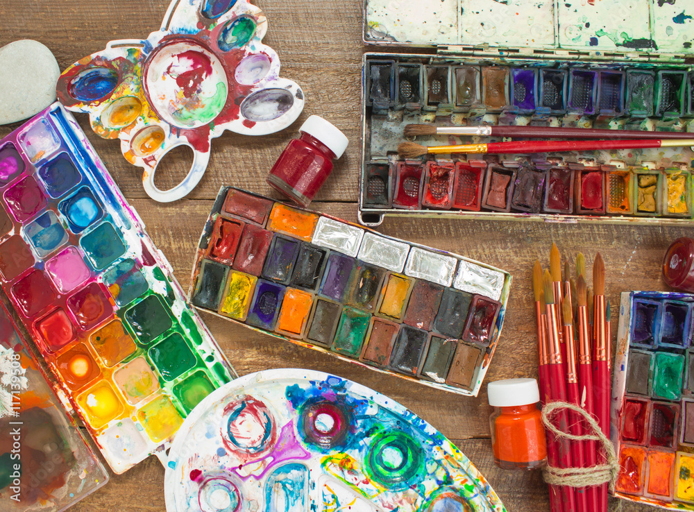 Watercolor paints, brushes and palette on wooden background. The workplace of the artist. Banner for school