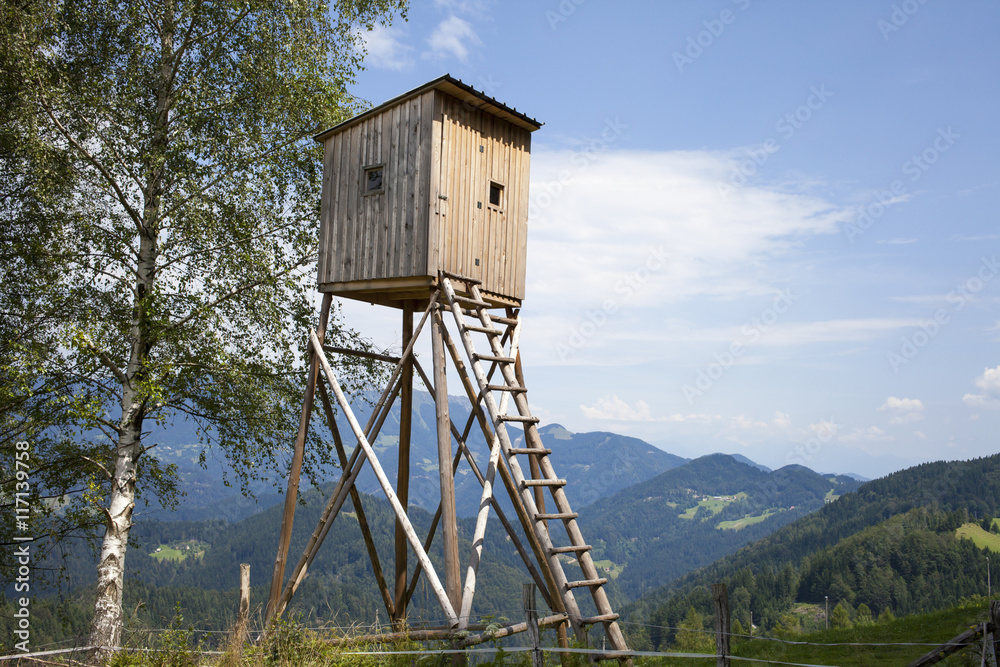 Hunters high tower. Wooden hunters high seat in the mountain forest, against blue sky Hunters high tower. Wooden hunters high seat in the mountain forest, against blue sky