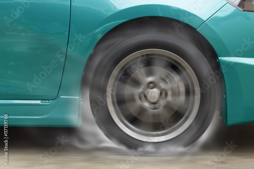 Green car racing spinning wheel burns rubber on floor. © jayzynism