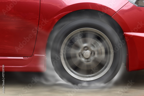 Red car racing spinning wheel burns rubber on floor. © jayzynism