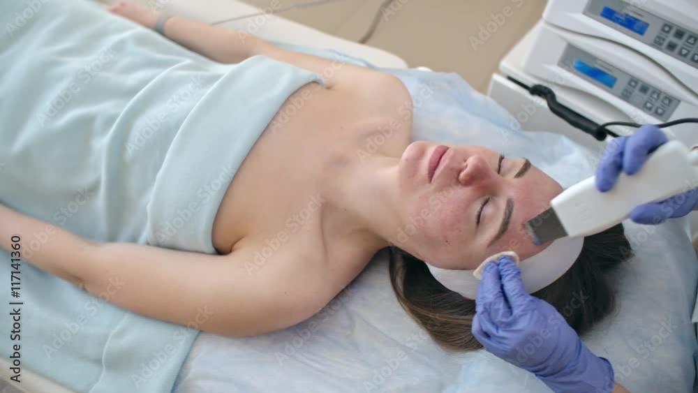 Woman lying on the couch in spa salon while cosmetician peeling skin on her face with ultrasonic scrubber Woman lying on the couch in spa salon while cosmetician peeling skin on her face with ultrasonic scrubber