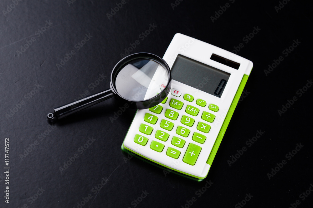 Calculator with a magnifying glass on a black background Calculator with a magnifying glass on a black background