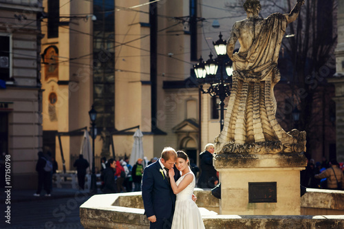 Thoughtful wedding couple pose behind an old fountain on the cit