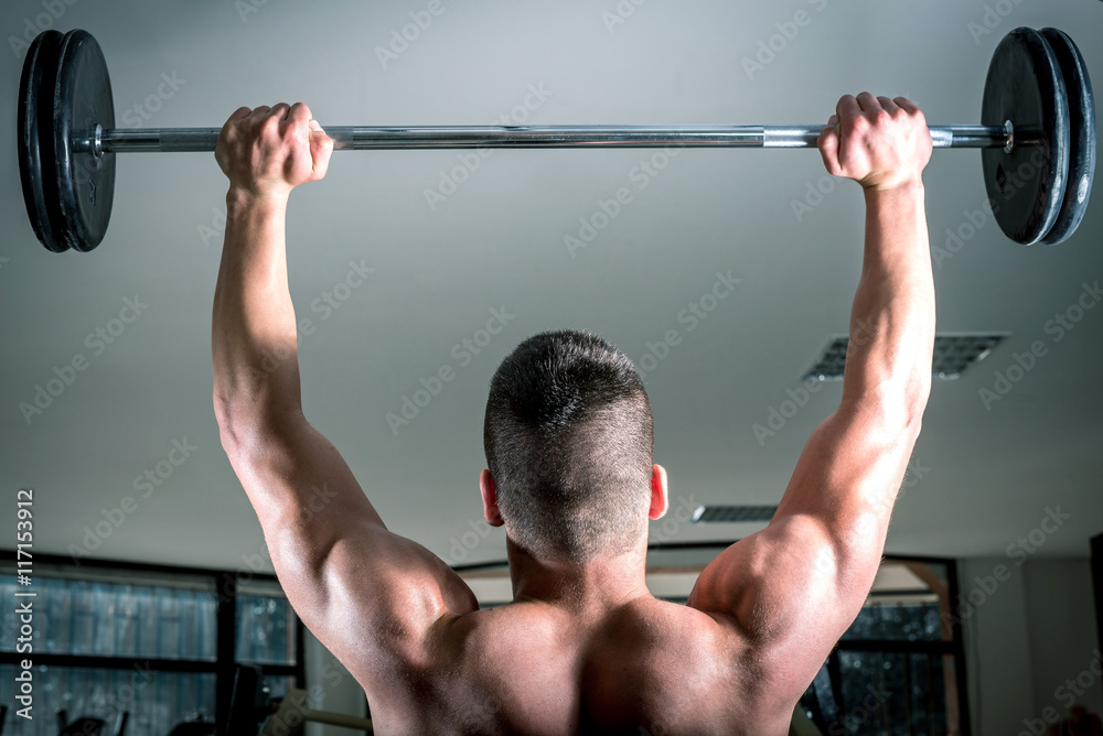 Naklejka premium Young man lifting barbell. View from behind.
