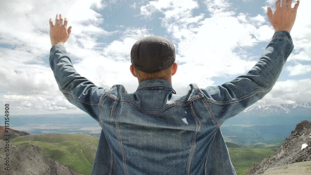 Hiker with backpack standing on top of a mountain with raised hands and enjoying sunrise Hiker with backpack standing on top of a mountain with raised hands and enjoying sunrise