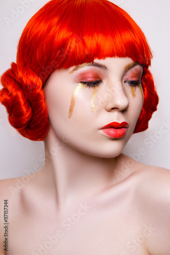 Woman in red and gold fashion make up and red hair on white background in studio photo. Art beauty photo