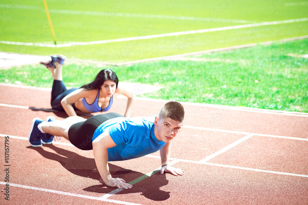 Fototapeta premium Young couple doing push ups on track.