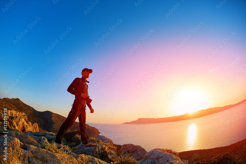 man standing on a cliff against a blue sea at the sunset