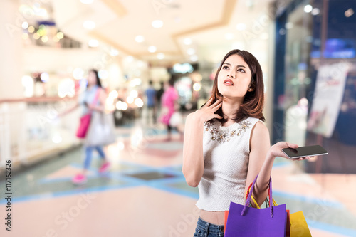 young woman is deciding something in a shopping mall with people concept and shopping bags over mall background