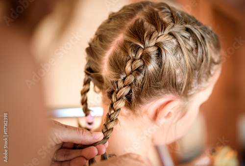 Mother is making of braids on little daughter's head.