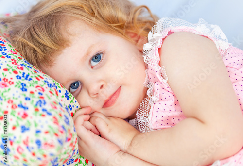 Little cute curly girl lies in a baby bed and a hand under her cheek. Face close up.