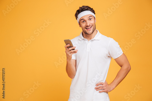 Happy young sportsman standing and using smartphone