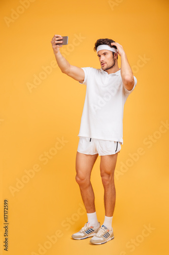 Smiling young sportsman standing and taking selfie with mobile phone