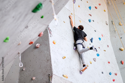 man climbing on artificial boulders wall indoor, rear view