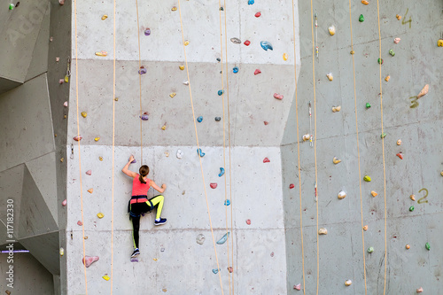 Beautiful young woman starts to climbing big artificial wall