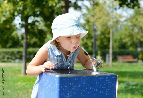 Cute baby girl drinking from water drinking fountain in summer
