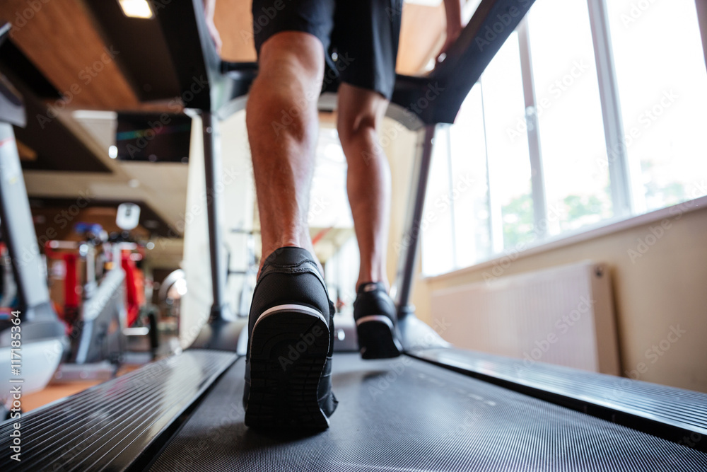 Back view of young sportsman running on treadmill in gym Back view of young sportsman running on treadmill in gym