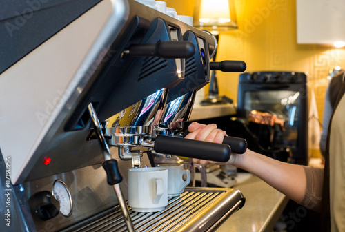 A barista prepares a hot shot of espresso, the coffee dripping down from a nice espresso machine in a coffee shop. Horizontal image.