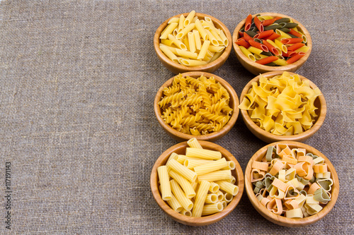 Various combinations of pasta on wooden background, burlap bags, bamboo bowls. diet and nutritional concept.