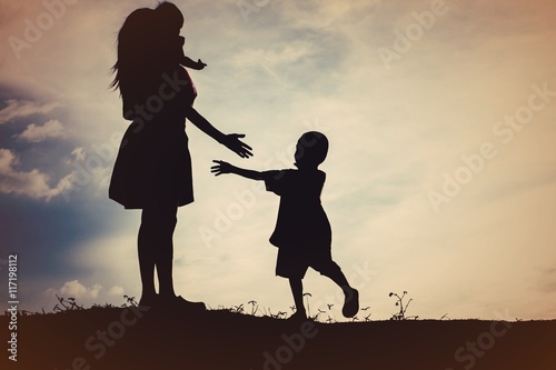 Mother holding baby walking on the sunset background.