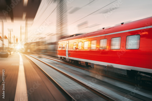 Modern high speed red passenger train moving through railway station in the evening. Railway station at sunset in Nuremberg, Germany. Railroad with motion blur effect. Industrial concept landscape