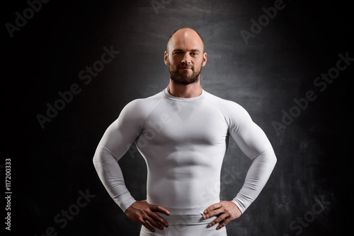 Young powerful sportsman in white clothing over black background.