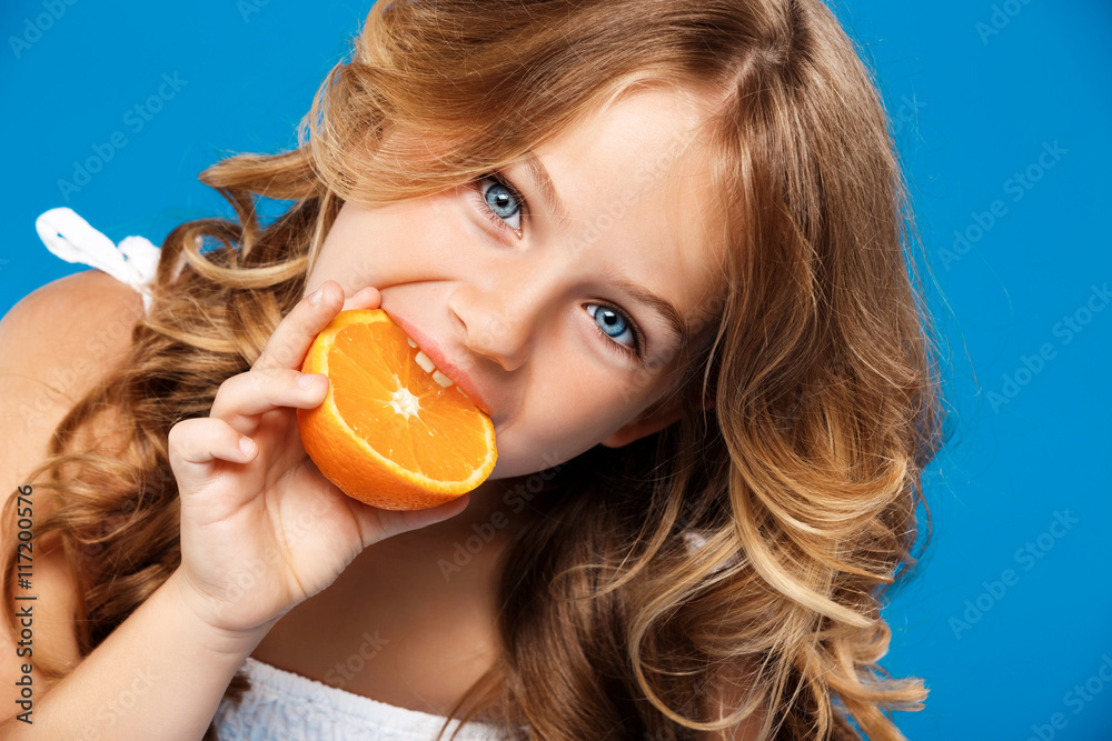 Young pretty girl eating orange over blue background. Young pretty girl eating orange over blue background.