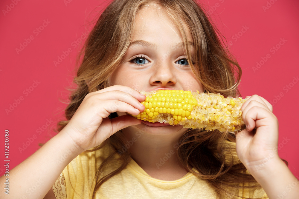 Young pretty girl eating corn over pink background. Young pretty girl eating corn over pink background.