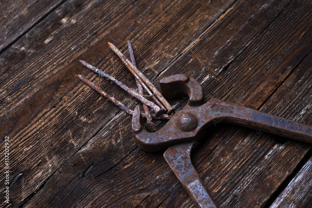 old rusty tongs with nails on wooden boards background old rusty tongs with nails on wooden boards background