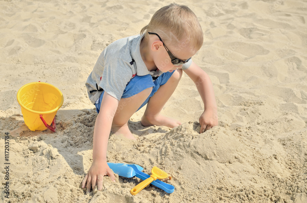 Little boy playing on the beach in the sand. Child sculpts figures out of the sand. Activities in the summer on the sea. Little boy playing on the beach in the sand. Child sculpts figures out of the sand. Activities in the summer on the sea.