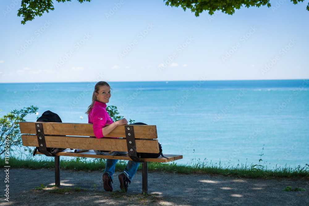 Young beautiful woman sitting on a bench on the lake shore and w Young beautiful woman sitting on a bench on the lake shore and w