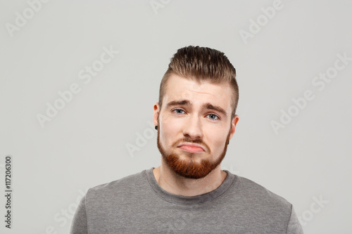 Upset young handsome man posing over grey background. Copy space.