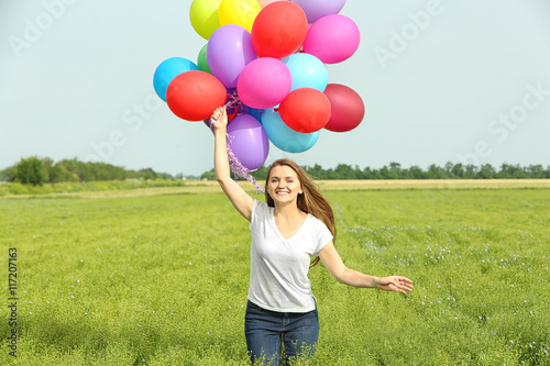 Happy woman with colorful balloons in field on blue sky background