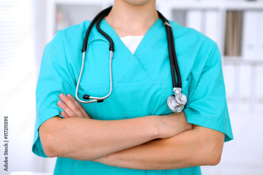 Female surgeon doctor is standing with arms crossed at hospital.  Physician  is ready to examine patient