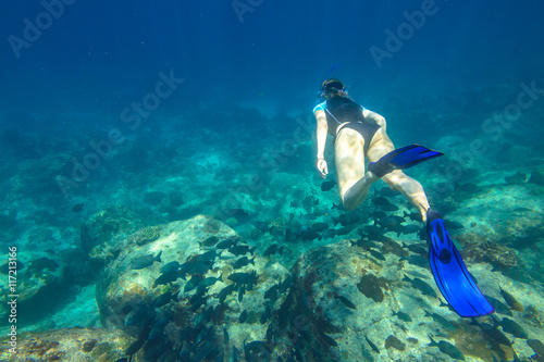 Young woman free diving in the blue waters of the popular Similan Islands in Thailand, Andaman Sea. On background a lot of fish.