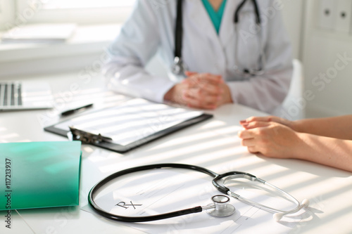 Stethoscope next to hand of doctor reassuring her female patient. Medical ethics and trust concept