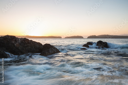 Long exposure picture of the waves crashing on the rocky beach in Vancouver Island, British Columbia, Canada, during sunset.