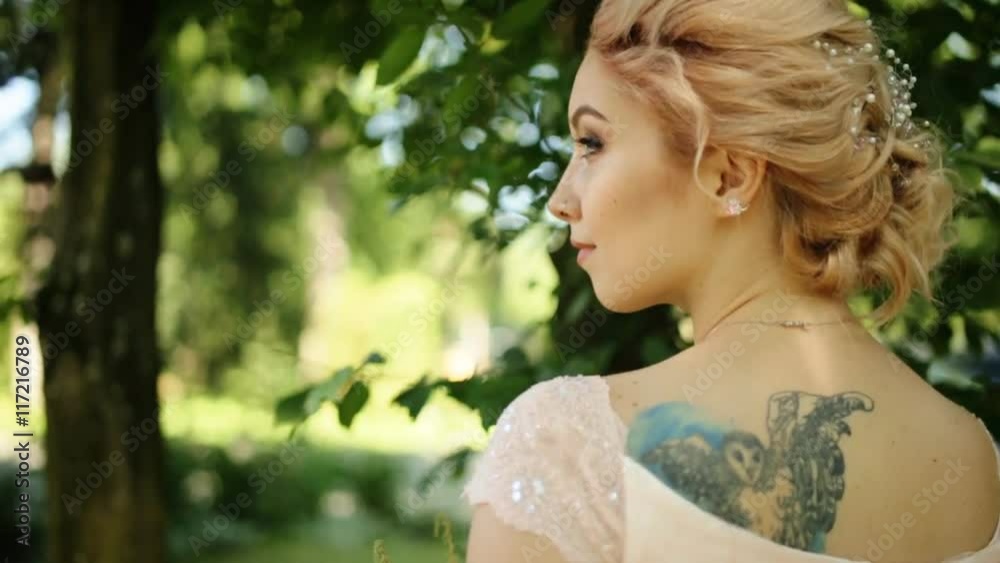 Smiling blonde bride with tattoo on her back and nose rang posing outdoors looking towards Smiling blonde bride with tattoo on her back and nose rang posing outdoors looking towards