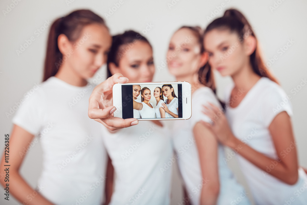 Positive friends portrait of four happy girls making selfie, sure funny faces, grimaces, joy, emotions, casual style, pastel colors, white wall. crazy funny woman. White background. Positive friends portrait of four happy girls making selfie, sure funny faces, grimaces, joy, emotions, casual style, pastel colors, white wall. crazy funny woman. White background.