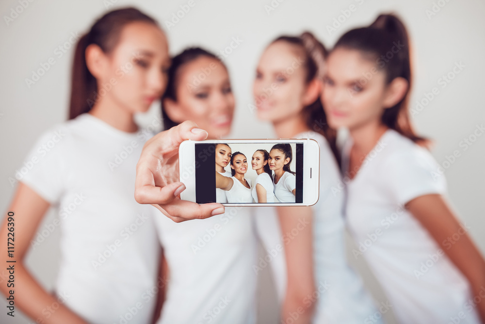 Positive friends portrait of four happy girls making selfie, sure funny faces, grimaces, joy, emotions, casual style, pastel colors, white wall. crazy funny woman. White background. Positive friends portrait of four happy girls making selfie, sure funny faces, grimaces, joy, emotions, casual style, pastel colors, white wall. crazy funny woman. White background.
