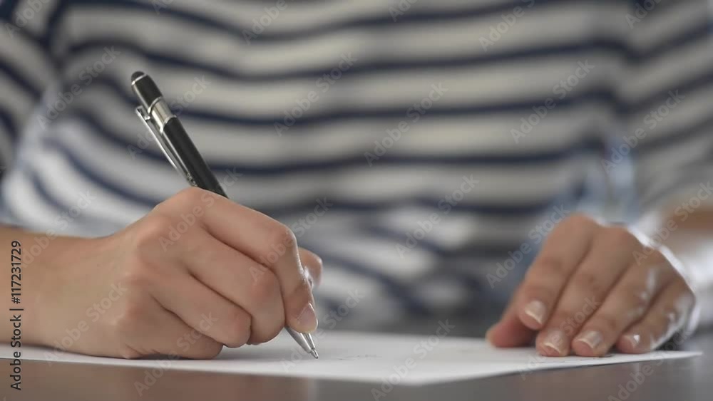Closeup of woman's hand writing on paper with pen