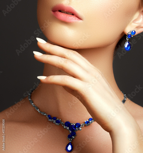 Elegant fashionable woman with jewelry. Beautiful woman with a sapphire necklace. Beauty young model with a diamond pendant on a gray background. Jewellery and accessories. Beauty and fashion concept