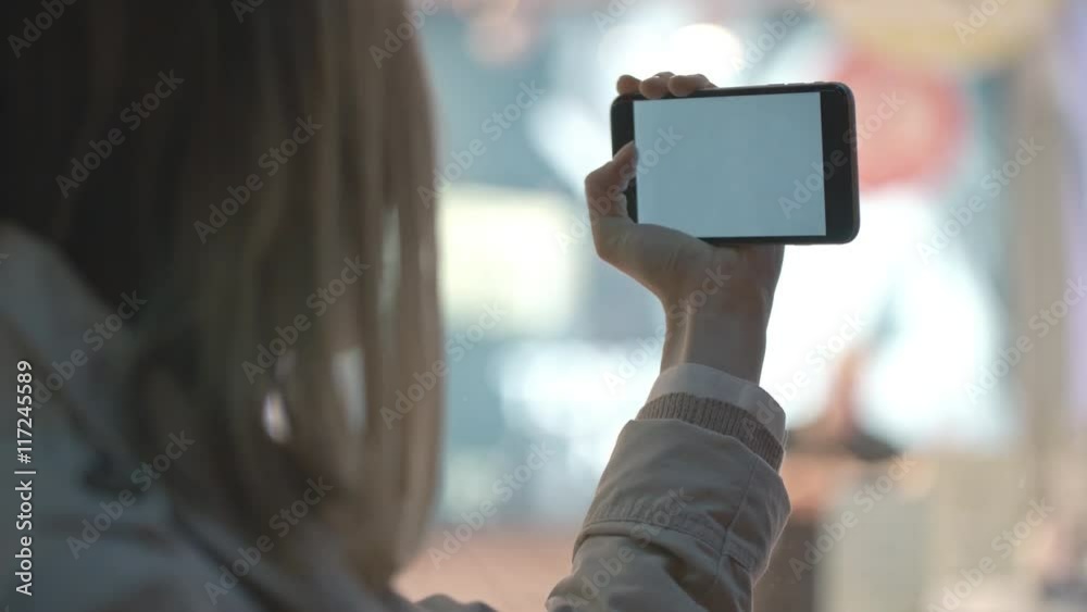 Blonde woman smiling and grimacing at her mobile phone camera and pressing button on touch screen to take a selfie
