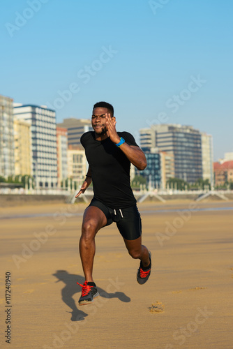 Black fit man running and sprinting at city beach. Athlete training outdoor.
